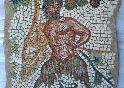 Mosaico Fauno | Arte del Mosaico en piedra. Realizado en técnica mixta, en Opus Vermiculatum y fondo en Opus Tessellatum. Representación de un fauno entre hojas de parra y un racimo de uvas.